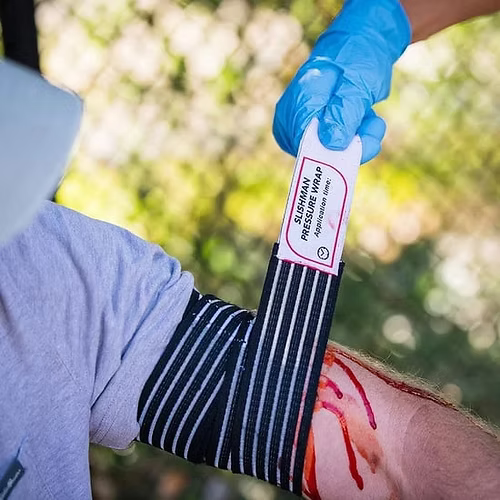Person applying a pressure wrap to an arm with a cut, outdoors.