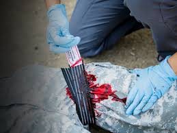 Person in blue gloves applying a bloodied slishman pressure wrap to a lower limb and on a concrete floor.