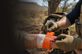 Tactical medic applying an orange Slishman Pressure Wrap to a casualty's wrist.